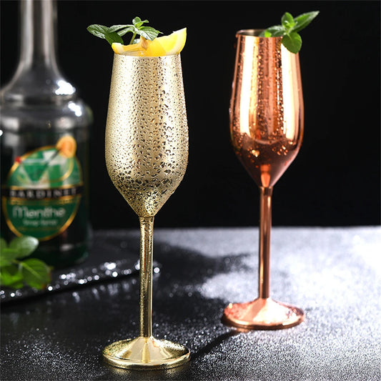 Two sparkling cocktails in gold and rose gold flutes with a bottle in the background.