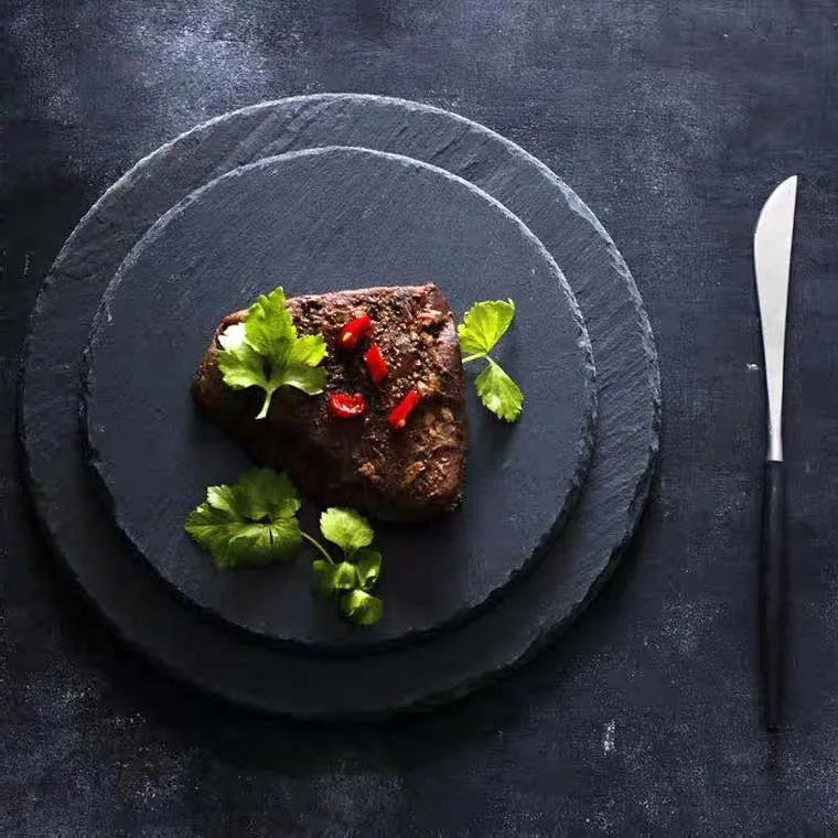 Serving of meat with garnishes on a slate plate with a knife on a dark background