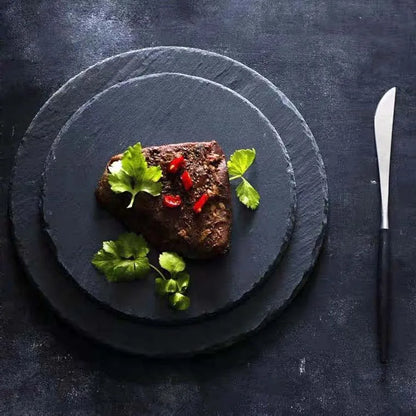 Serving of meat with garnishes on a slate plate with a knife on a dark background