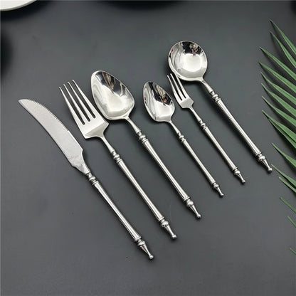 Set of silver cutlery including knives, forks, and spoons on a dark surface with green leaves.