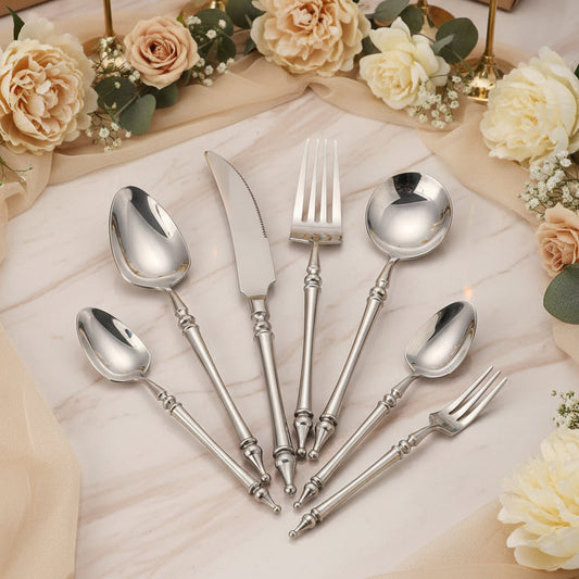 Set of silver cutlery on a black plate with vegetables in the background